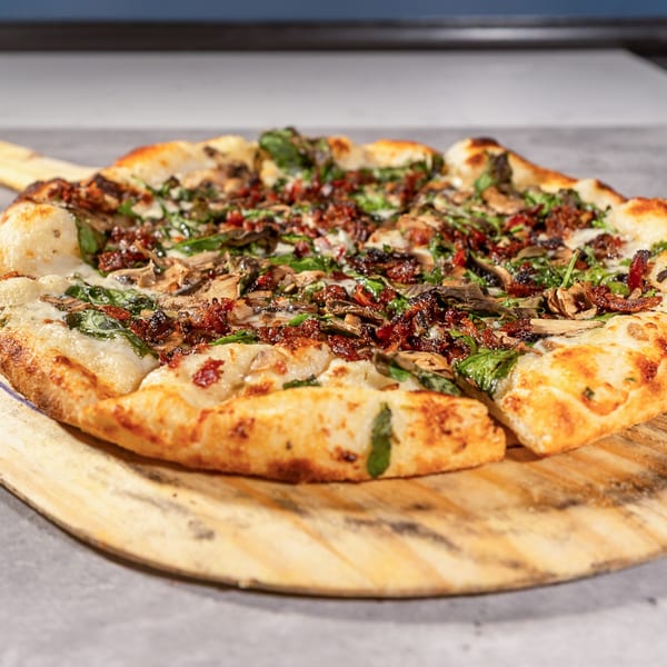 Twisted Sisters Tap House pizza with mushrooms, spinach, and bacon on a wooden peel.