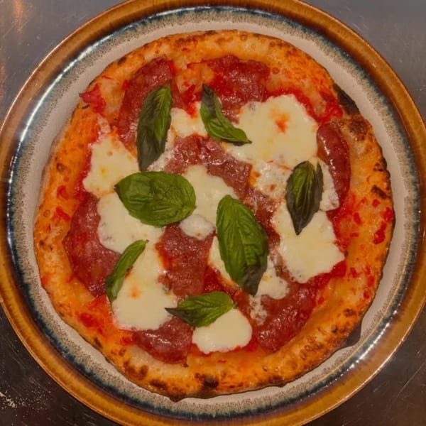 A Twisted Sisters Tap House pepperoni pizza with fresh mozzarella and basil on a rustic plate.