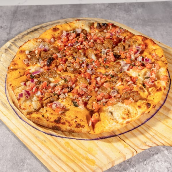 Twisted Sisters Tap House pizza with sausage, diced tomatoes, and red onions on a wooden peel.
