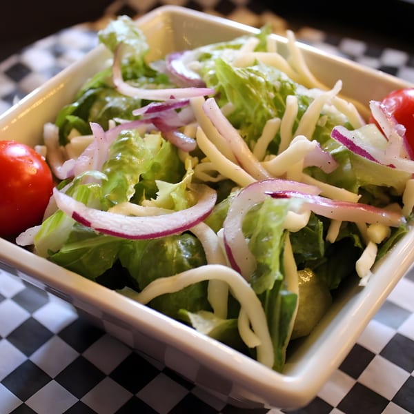 Fresh green salad with red onions, shredded cheese, and cherry tomatoes in a white bowl.