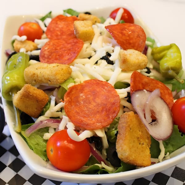 Close-up of a pizza salad with pepperoni, cheese, tomatoes, croutons, and peppers.