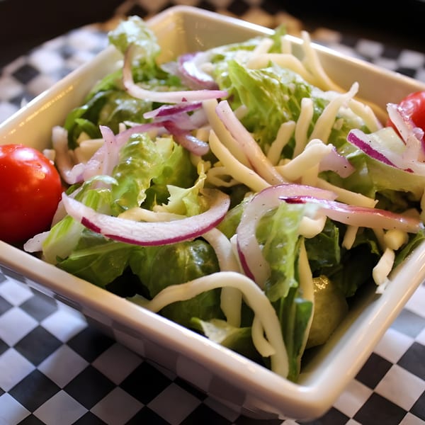 Fresh side salad with lettuce, red onion, shredded cheese, and cherry tomatoes in a white bowl.