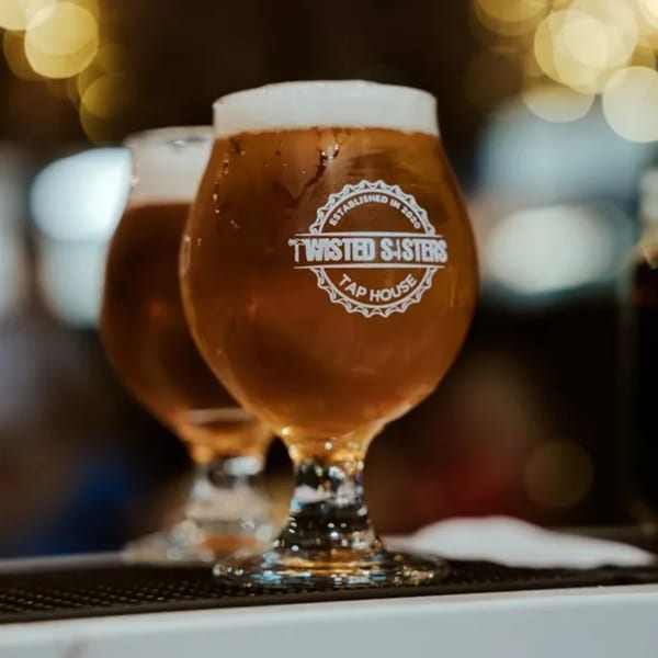 Two Twisted Sisters Tap House beer glasses filled with golden beer and foamy heads.