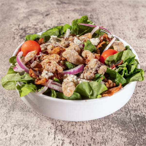 Spinach salad with crispy chicken, red onion, cherry tomatoes, and crumbled cheese in a white bowl.