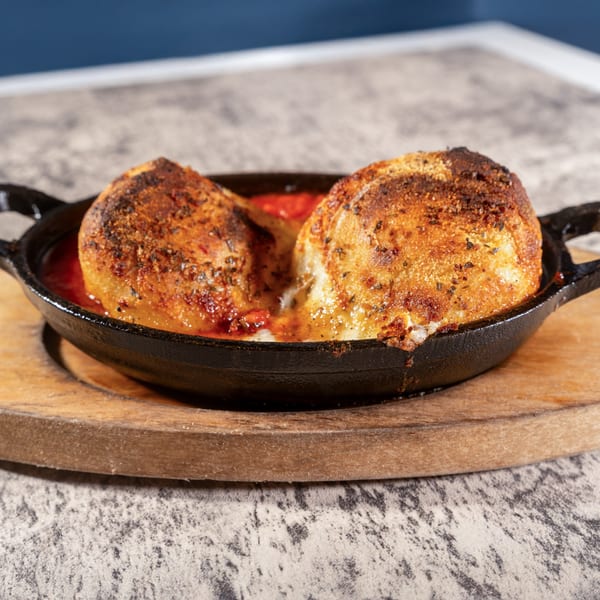 Two golden-brown baked dough balls in a cast iron skillet with red sauce and melted cheese.