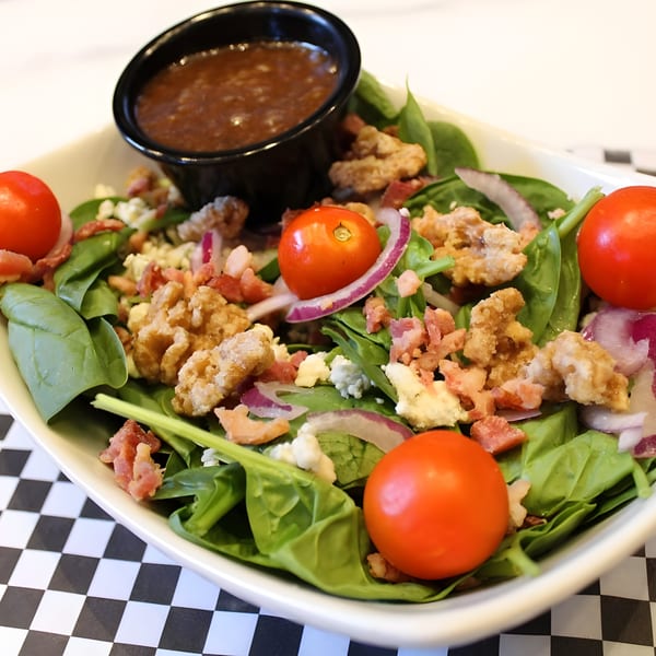 Spinach salad with cherry tomatoes, bacon, walnuts, red onion, and blue cheese crumbles, with dressing.