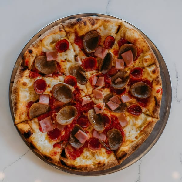 A Twisted Sisters Tap House pizza with pepperoni, sausage, and ham on a metal tray.