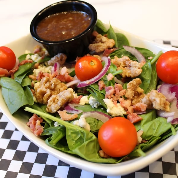 Spinach salad with cherry tomatoes, bacon, blue cheese, red onion, and fried chicken, with dressing.