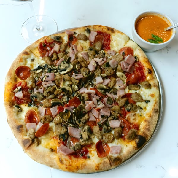 Twisted Sisters Tap House pizza with pepperoni, ham, sausage, and mushrooms, next to a bowl of tomato soup.