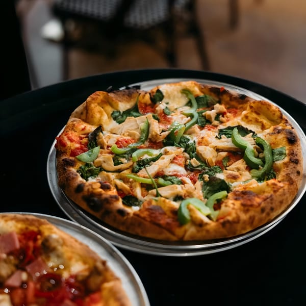 A Twisted Sisters Tap House pizza with chicken, green peppers, and spinach on a dark table.
