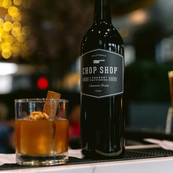 A bottle of Chop Shop Cabernet Sauvignon wine next to a cocktail with a cinnamon stick and walnuts.