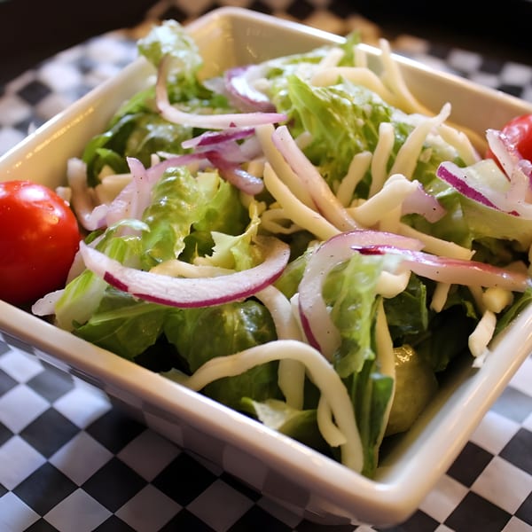 Fresh green salad with red onions, shredded cheese, and cherry tomatoes in a white bowl.
